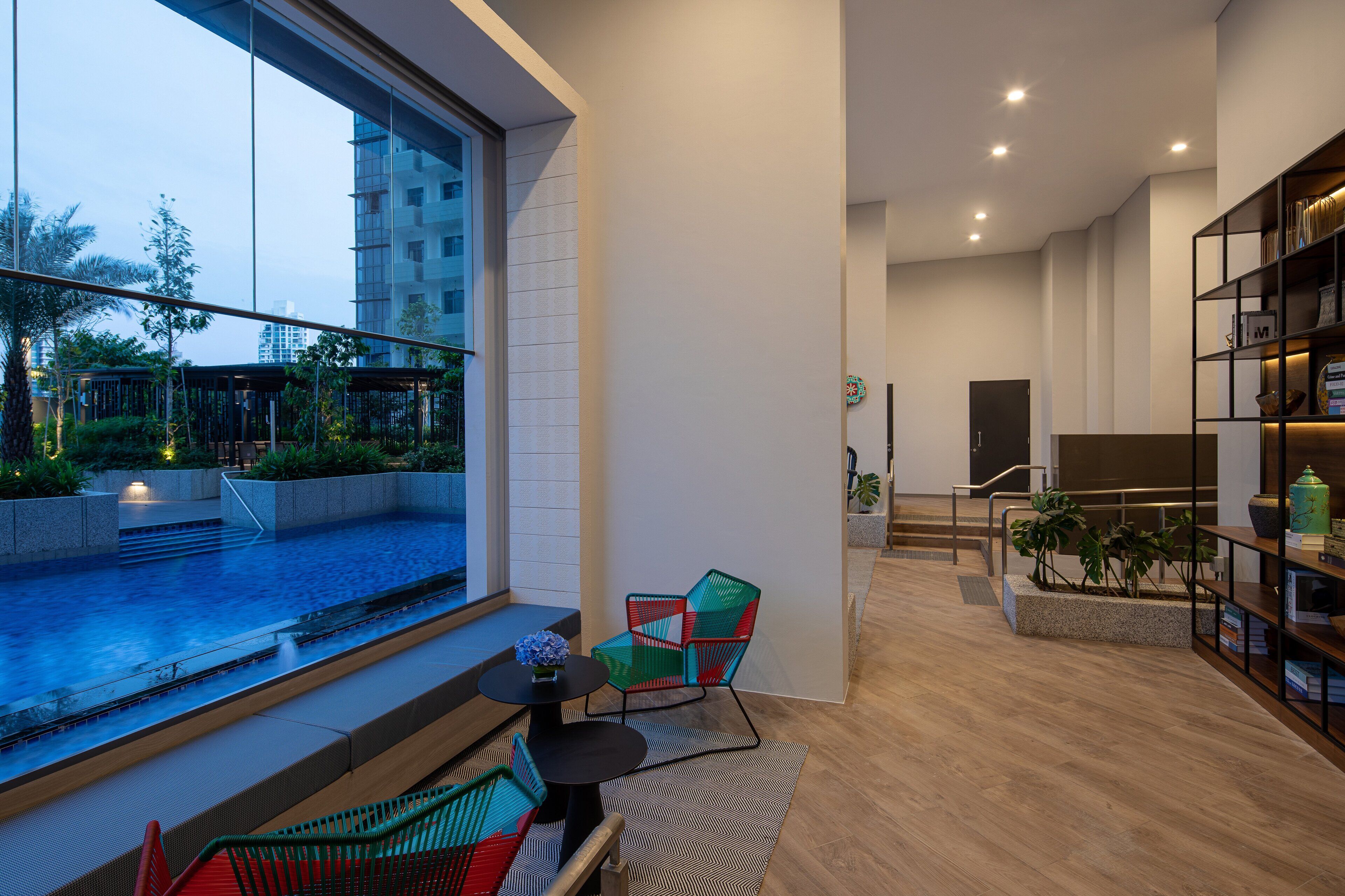 A modern living room with a large window overlooking a pool, a staircase, and a bookshelf.