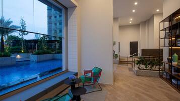 A modern living room with a large window overlooking a pool, a staircase, and a bookshelf.