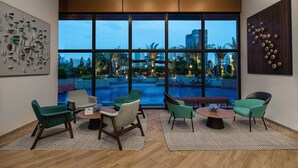 A modern lounge area with large windows, multiple seating options, and a view of a pool and cityscape. - Citadines Balestier Singapore (Singapore)