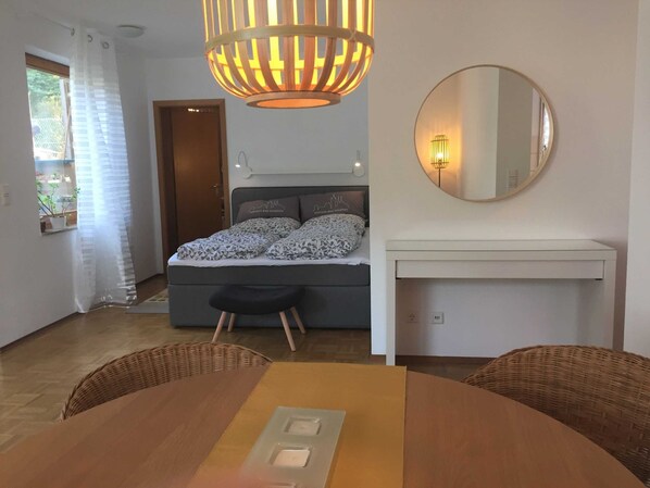 A bedroom with a bed, bedside table, mirror, and a dining area with a table and chairs.