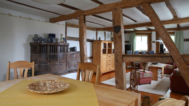 Una camera rustica con travi in legno, un tavolo da pranzo con un sottotavolo, sedie, un mobile contenitore con stoviglie e un’accogliente zona salotto con un divano e poltrone.