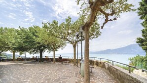 Een terras met stenen bestrating, banken en bomen, met uitzicht op een waterpartij en verre bergen.