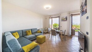 Een moderne woonkamer met een grijze bank, gele kussens, een klein tafeltje en een televisie.