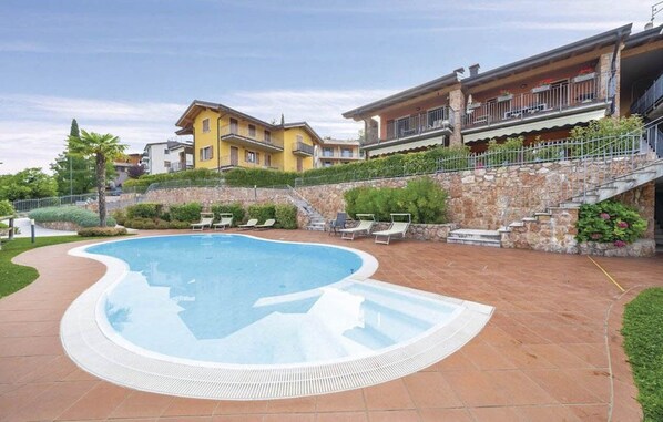 En swimmingpool med stenvæg, omgivet af en terrasse med liggestole.