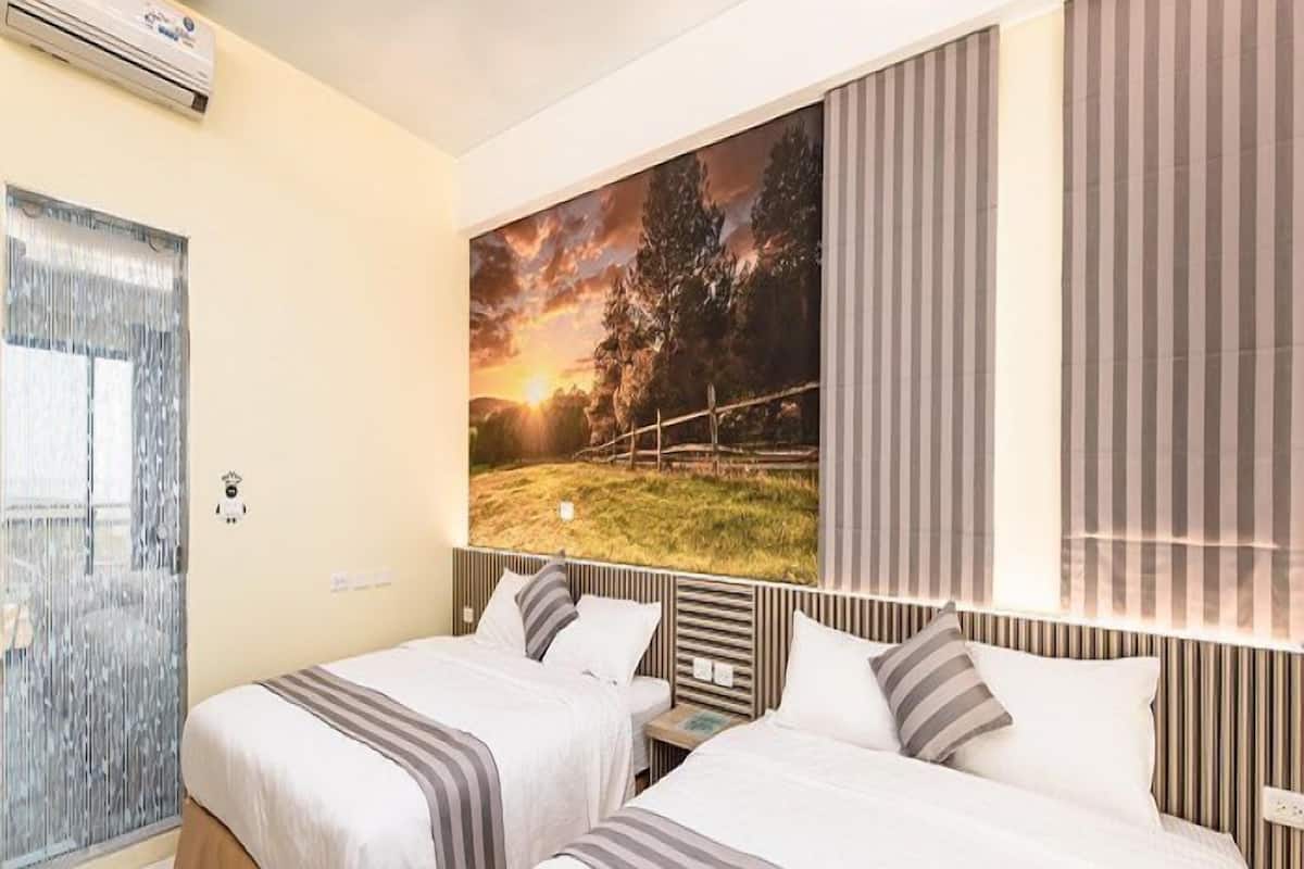 A hotel room with two beds, a large window with curtains, an air conditioning unit, and a painting of a sunset landscape.