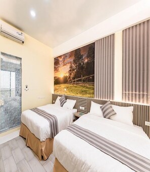 Une chambre d’hôtel avec deux lits, une grande fenêtre avec des rideaux, un appareil de climatisation et un tableau représentant un paysage au coucher du soleil.