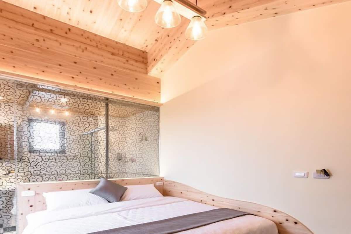 A bedroom with a wooden ceiling, a bed with a headboard, and a window with a decorative pattern.