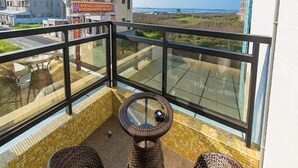 A balcony with wicker chairs and a glass table, overlooking a beach and buildings. - Tiamo B&B (Magong)