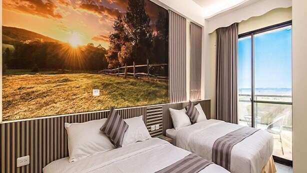 A hotel room with two beds, a large scenic mural on the wall, and a view of the sea through a large window. - Tiamo B&B (Magong)