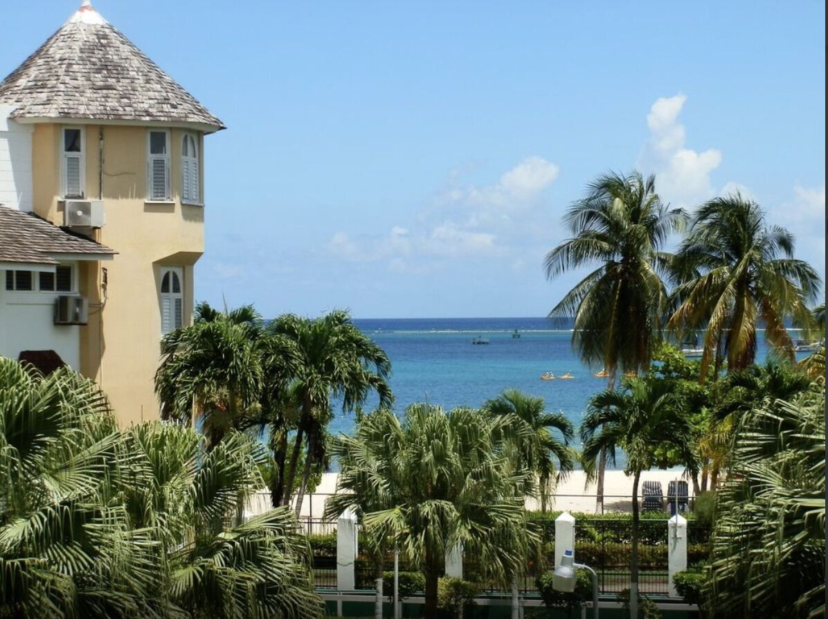 A coastal view with a yellow building, palm trees, and a clear blue sea.