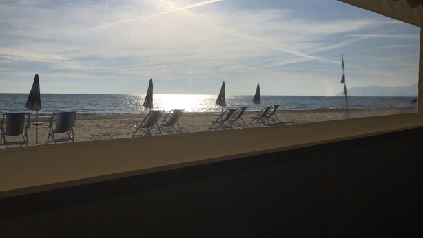 On peut admirer la plage depuis l’intérieur d’un bâtiment, avec des chaises de plage et des parasols alignés le long du rivage.