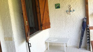 Une pièce avec un plafond en bois, un sol carrelé de carreaux blancs, une table blanche et une fenêtre avec des volets en bois.