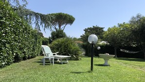 Un jardin bien entretenu, avec une pelouse, un fauteuil de jardin blanc, un abreuvoir pour oiseaux et un lampadaire.