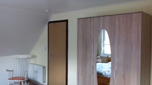 Un dormitorio con techo inclinado, un armario de madera, una silla y una cama con ventana.
