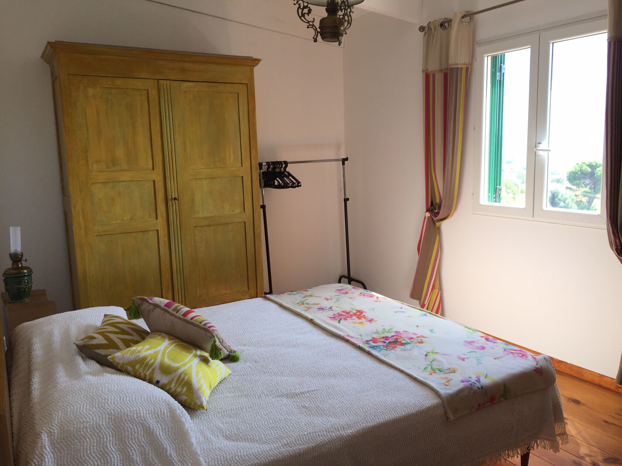 Ein Schlafzimmer mit Bett, Kleiderschrank, Kleiderstange und einem Fenster mit Vorhängen.