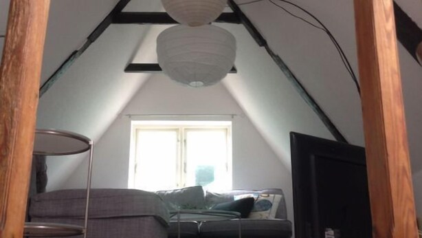 A loft bedroom with a sloped ceiling, exposed wooden beams, a bed, a desk, and a window with natural light. - listed family home, close to Gottorf Castle  (Schleswig)