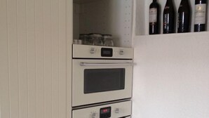 A kitchen with three white ovens, a wooden bowl on the upper shelf, and a wine rack with bottles. - listed family home, close to Gottorf Castle  (Schleswig)