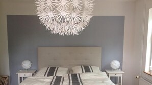 A bedroom with a tufted headboard, two bedside tables with decorative items, and a white bedspread with black stripes. - listed family home, close to Gottorf Castle  (Schleswig)