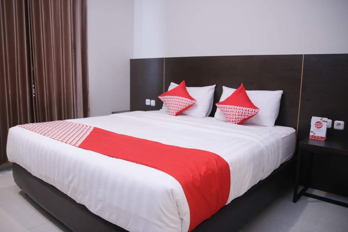 A hotel room with a large bed, a dark headboard, and a red and white bedspread.