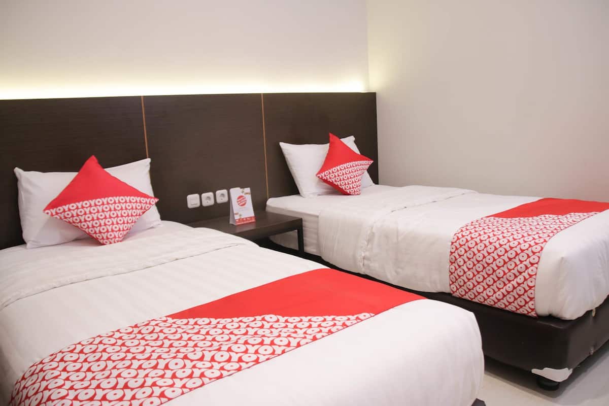 A hotel room with two beds, each with a red and white patterned bedspread, a dark headboard, and a bedside table with a card.