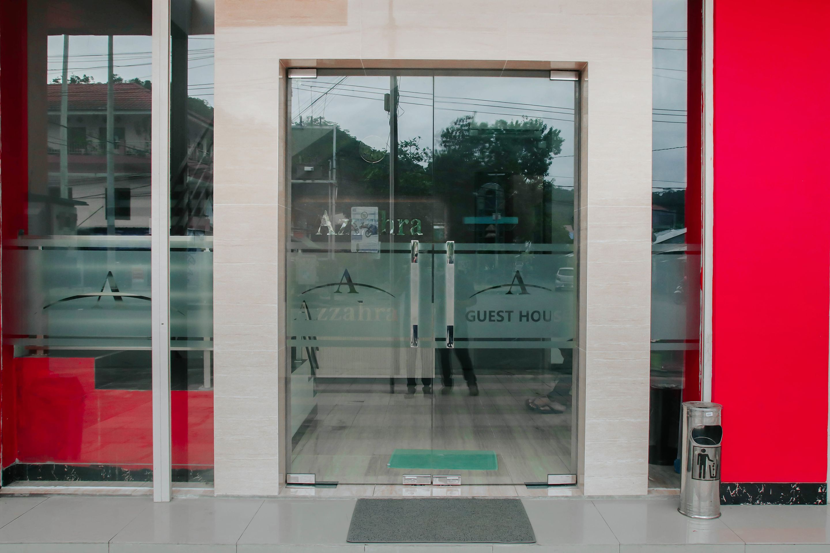 A hotel entrance with a glass door, a red wall, and a metal trash can.