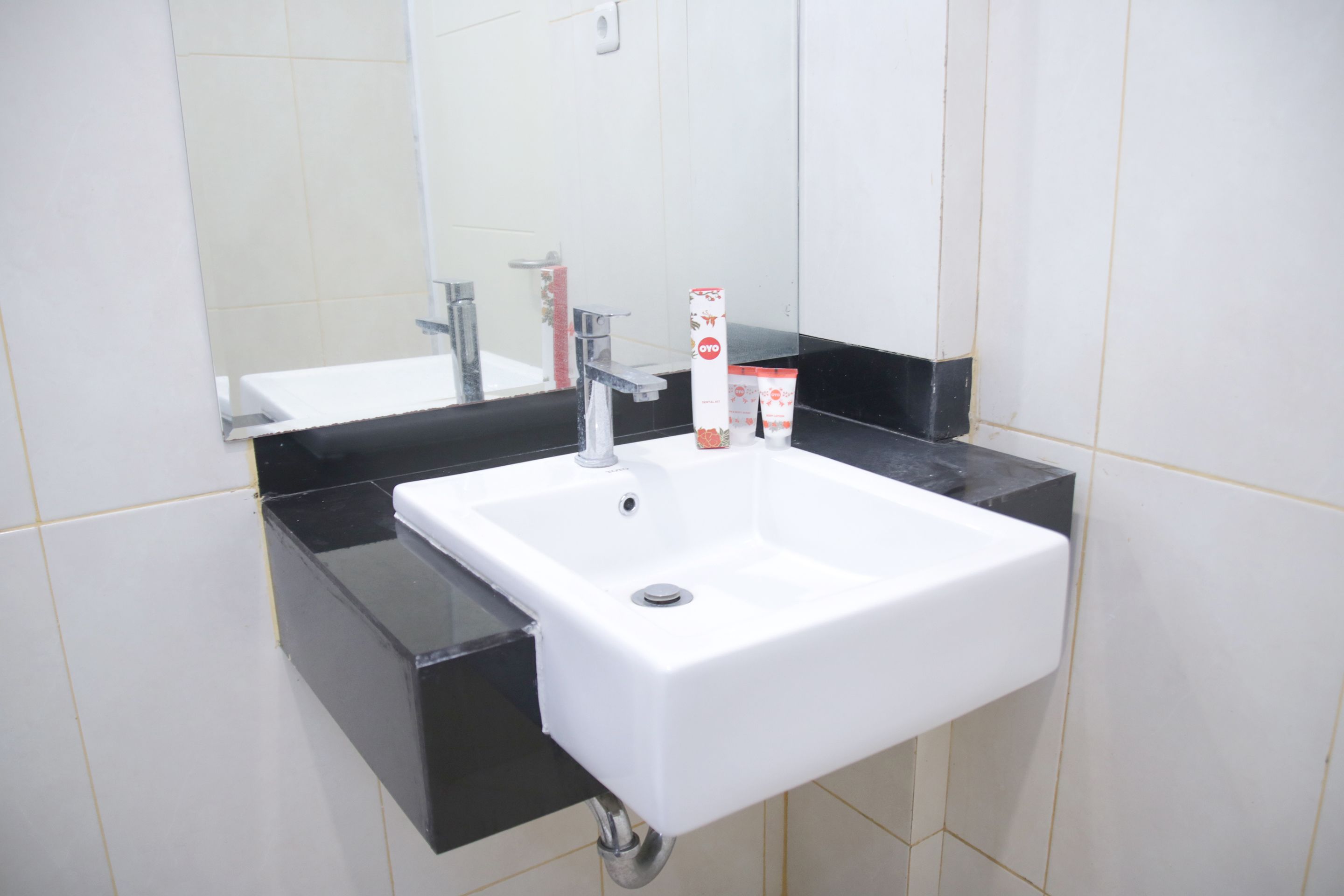 Un lavamanos blanco con encimera negra, un espejo encima y una pared de azulejos blancos.