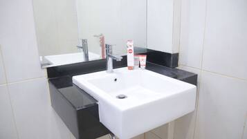 Un lavamanos blanco con encimera negra, un espejo encima y una pared de azulejos blancos.