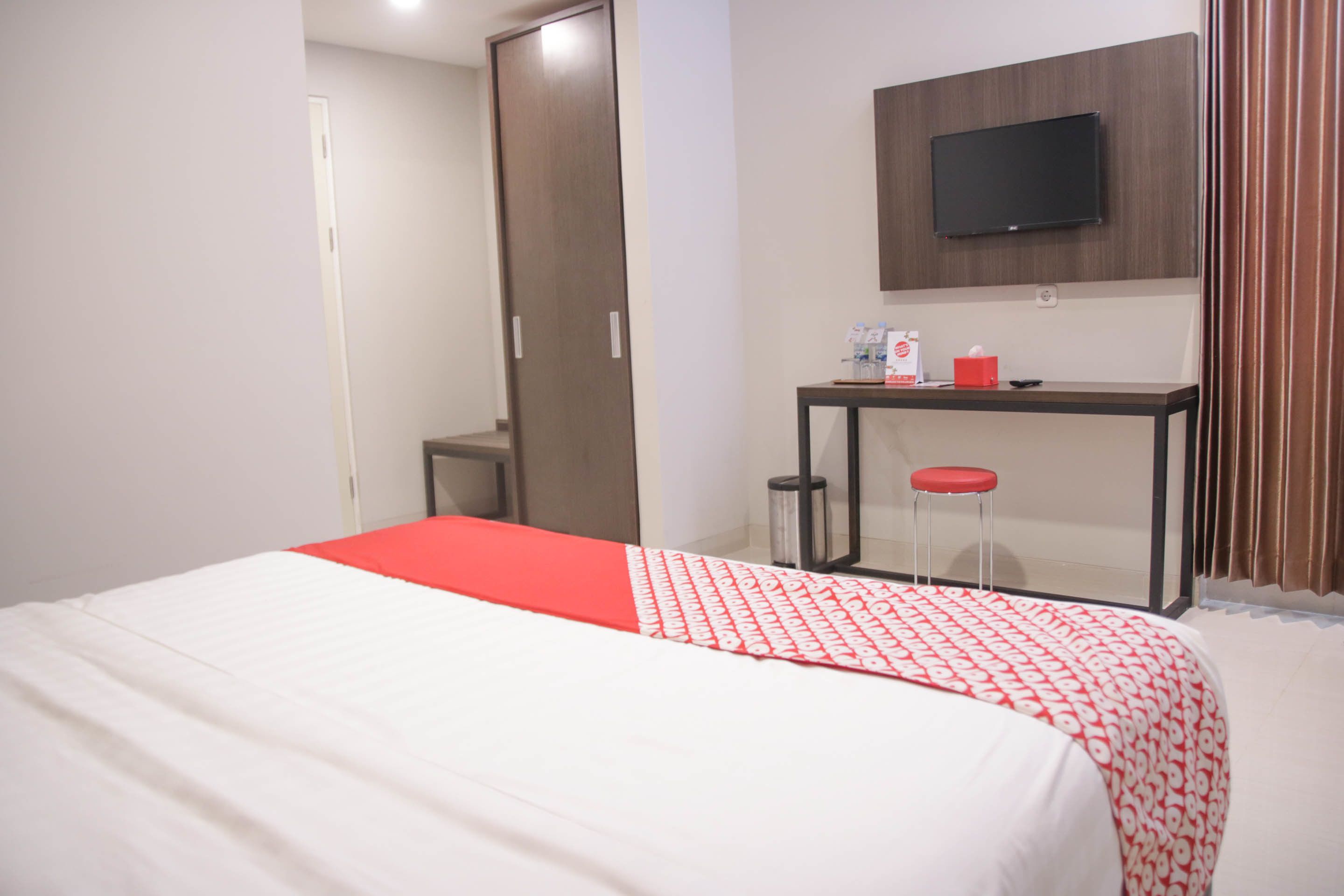 Una habitación de hotel con cama, escritorio, televisor y ventana con cortinas.