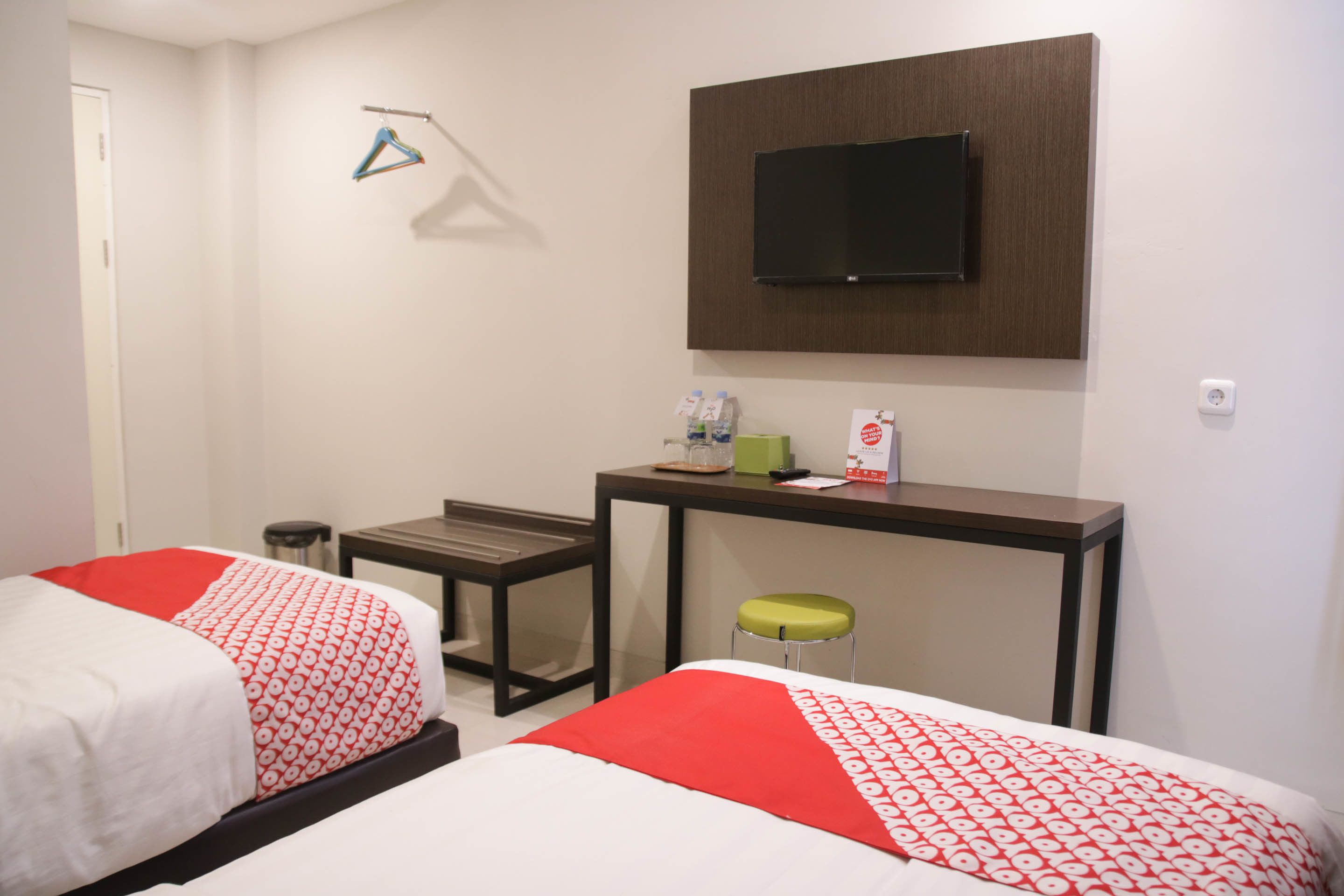 A hotel room with two beds, a desk, a chair, a TV, and a small table with items on it.