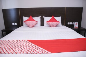 Een hotelkamer met een groot bed, twee rode kussens, een witrood beddegoed en een donker hoofdeinde.