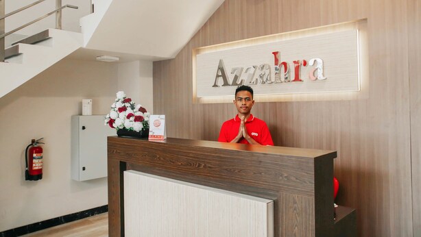 Un comptoir d’accueil d’hôtel avec un revêtement en bois, une horloge au mur et une enseigne sur laquelle on peut lire « Azzahra ».