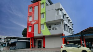 Un immeuble à plusieurs étages, doté d’une façade rouge et verte, avec une entrée bien visible et une voiture garée devant.