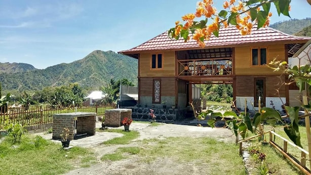 A two-story wooden house with a tiled roof, a stone staircase, and a view of mountains in the background. - Bale Sembahulun Cottages & Tent (Sembalunbumbung)
