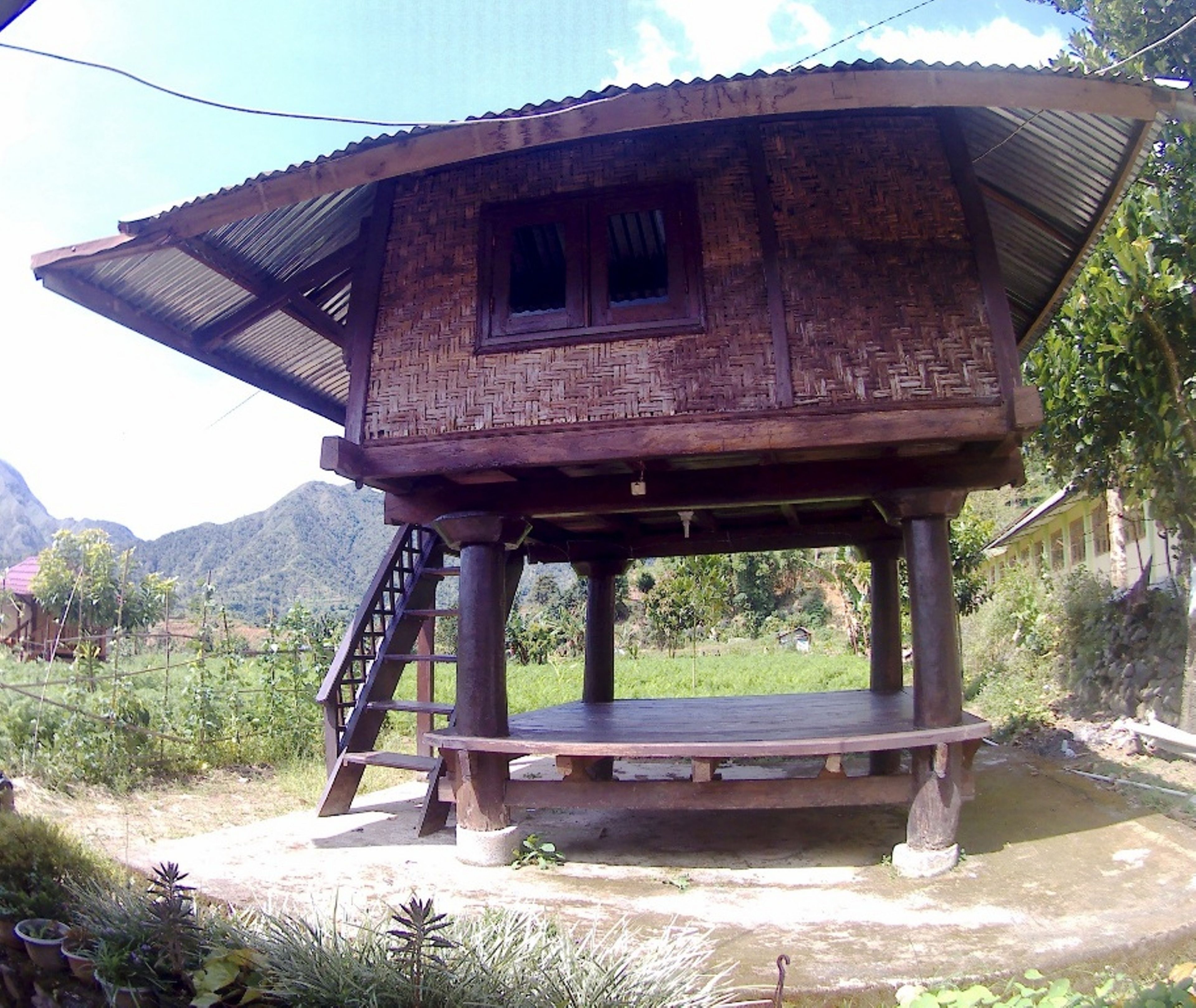 A rustic wooden house with a sloped roof, a small window, and a wooden staircase leading to a platform.