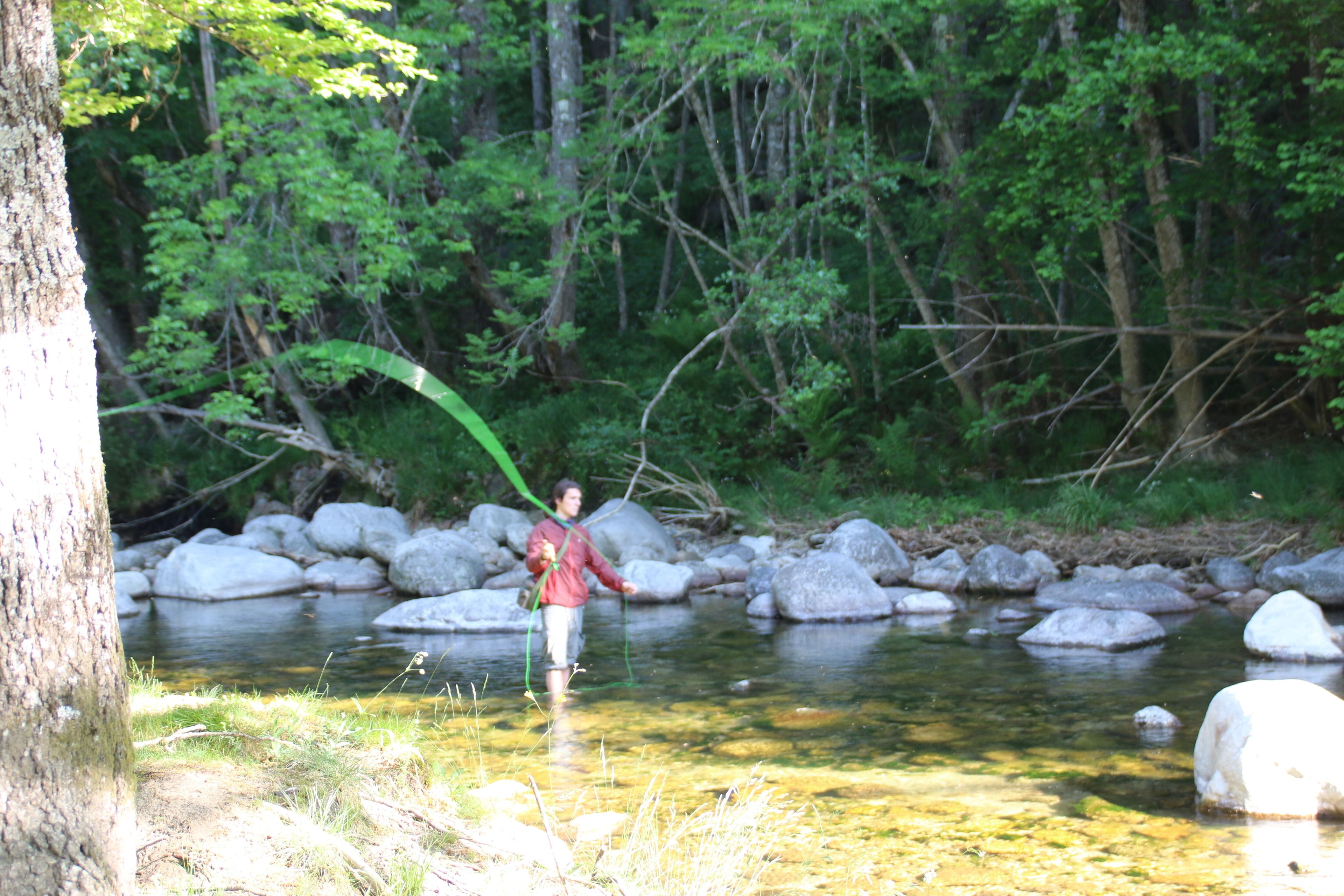 A person standing in a clear stream surrounded by rocks and trees.