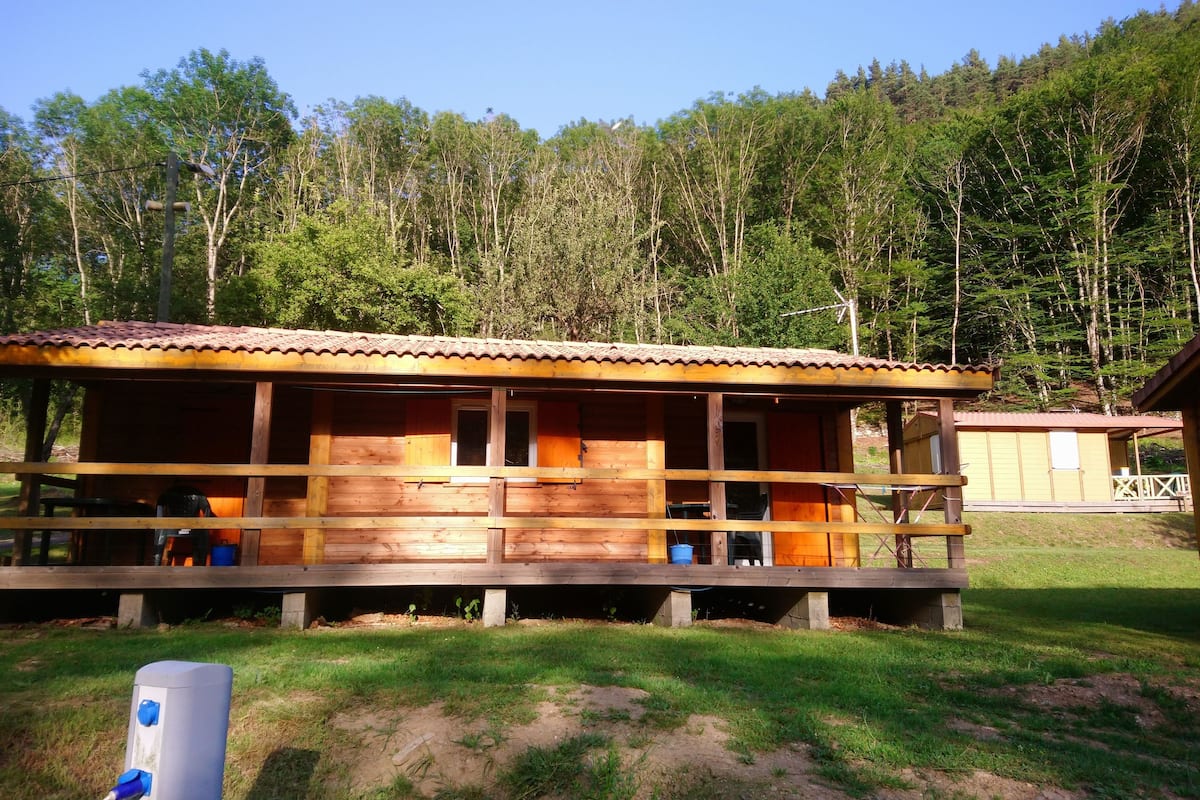 A wooden cabin with a porch, surrounded by a forest.