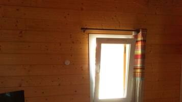 A small, cozy room with wooden walls and a sloped ceiling. It includes a bed, a desk with a chair, and a television.