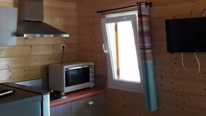 Cocina compacta con paredes de madera, microondas, estufa y ventana con cortinas.