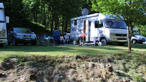Una vehículo recreativo (RV) estacionado en un área boscosa, con un campo de césped al frente.
