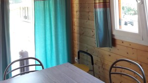 Interior de una cabaña de madera con una mesa de comedor, sillas y una ventana con cortinas.
