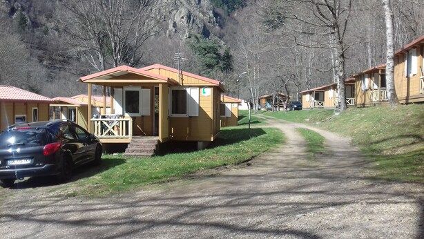 Un hilero de cabañas de madera con un sendero de grava que las conecta, rodeado de árboles y colinas.