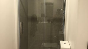 Cabina de ducha con paredes de vidrio y un inodoro blanco a la derecha.