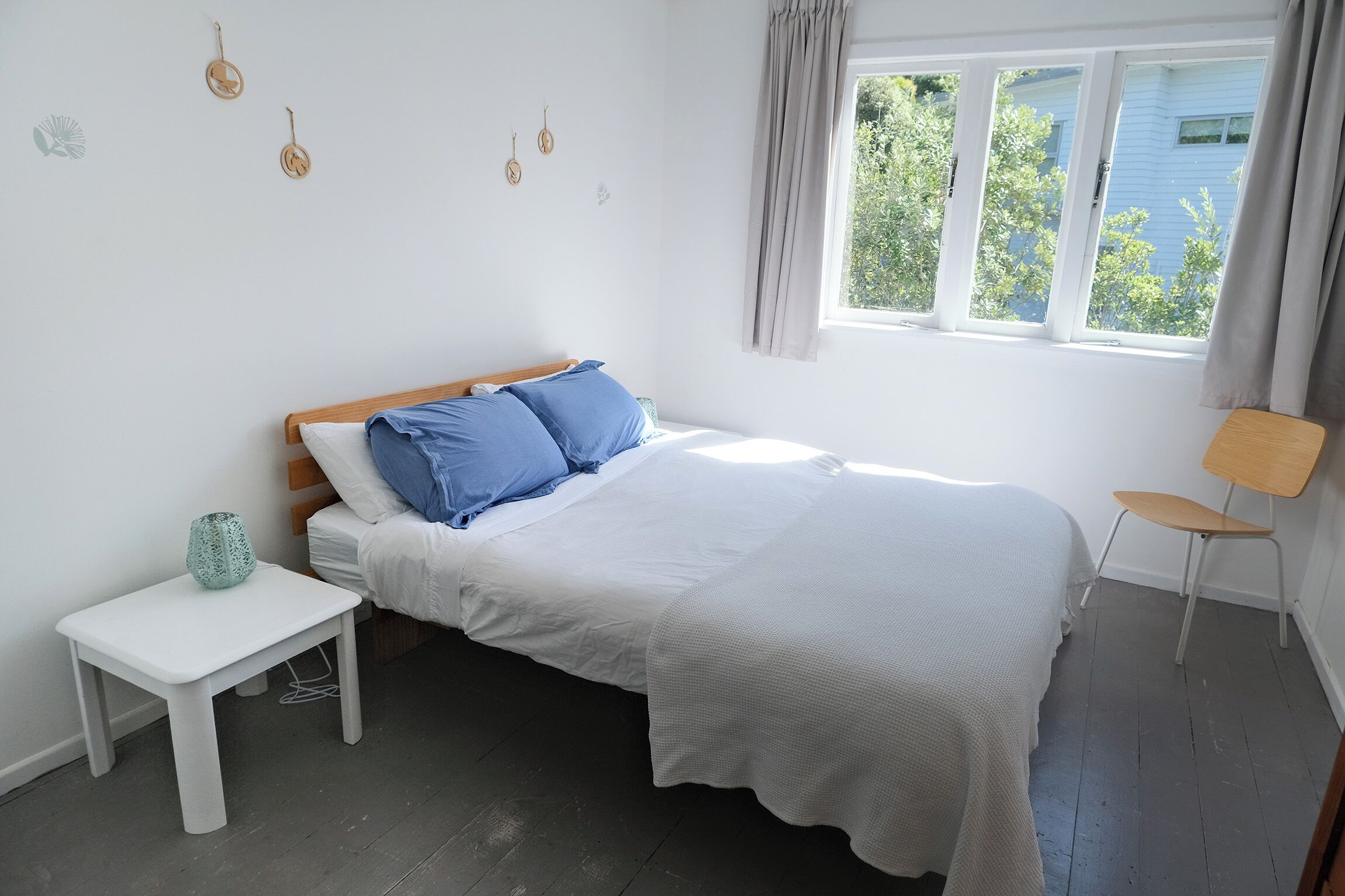 A bedroom with a bed, a small white table, a chair, and a window with curtains.