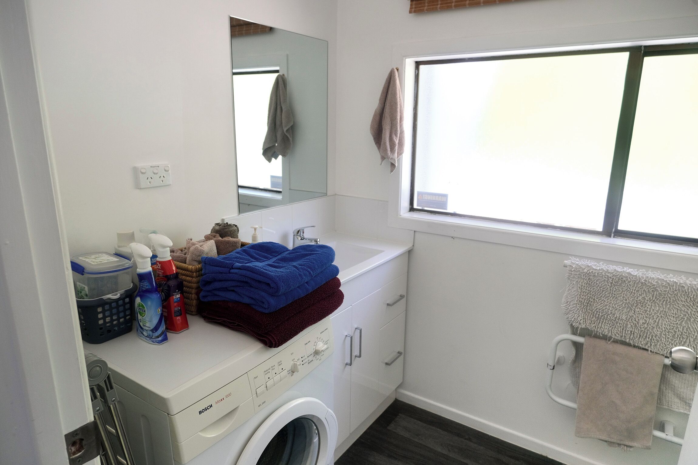 Un baño moderno con una lavadora Bosch, un lavamanos, un espejo y una ventana.