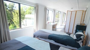 Habitació amb dos llits, un escriptori i vista a arbres a l'exterior.