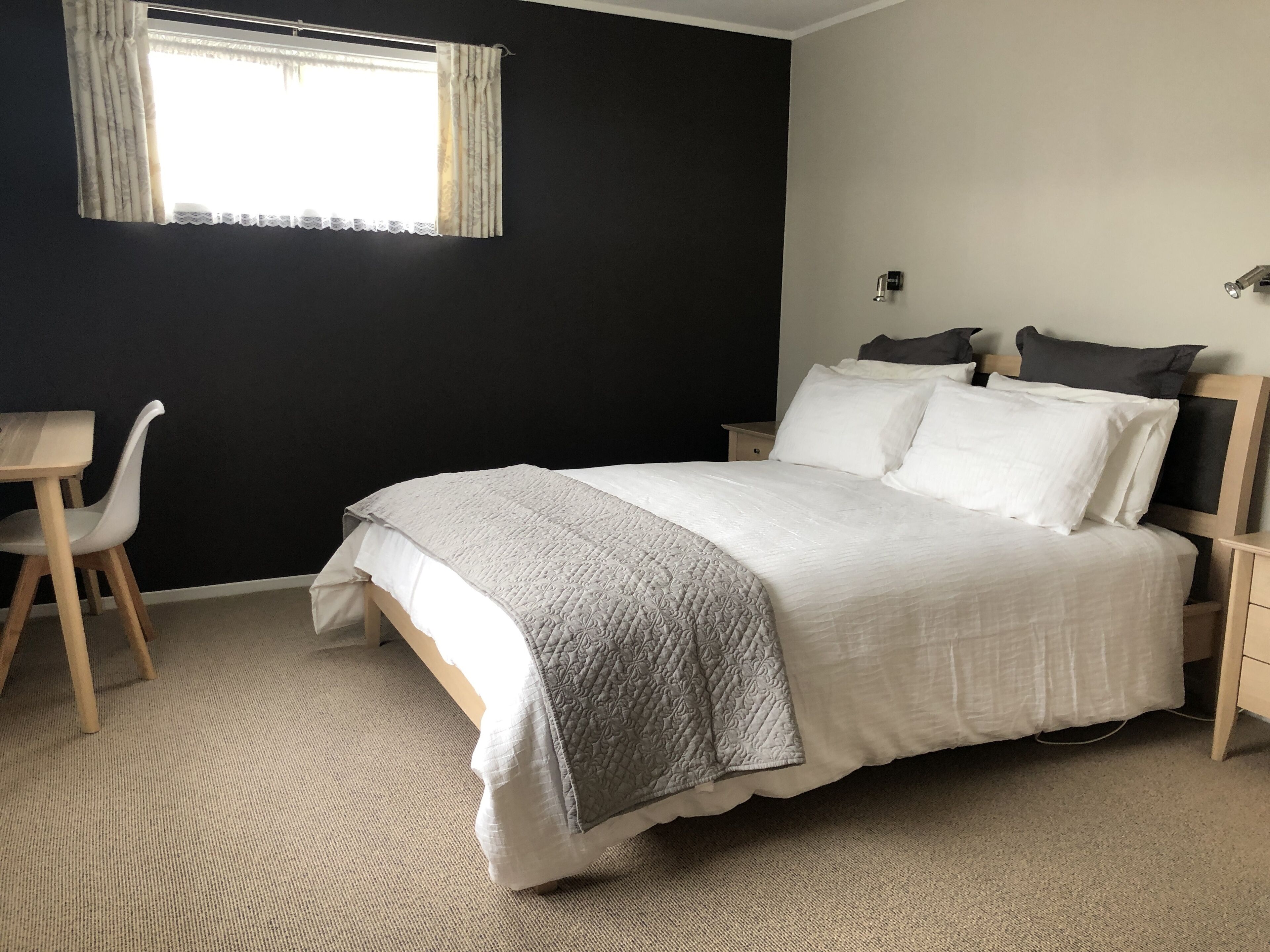 A bedroom with a bed, bedside tables, a chair, a window with curtains, and a wall-mounted light.