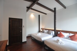 A hotel room with two beds, wooden beams on the ceiling, a door, and a small table. - The Eight Ratvithi House (Chiang Mai)