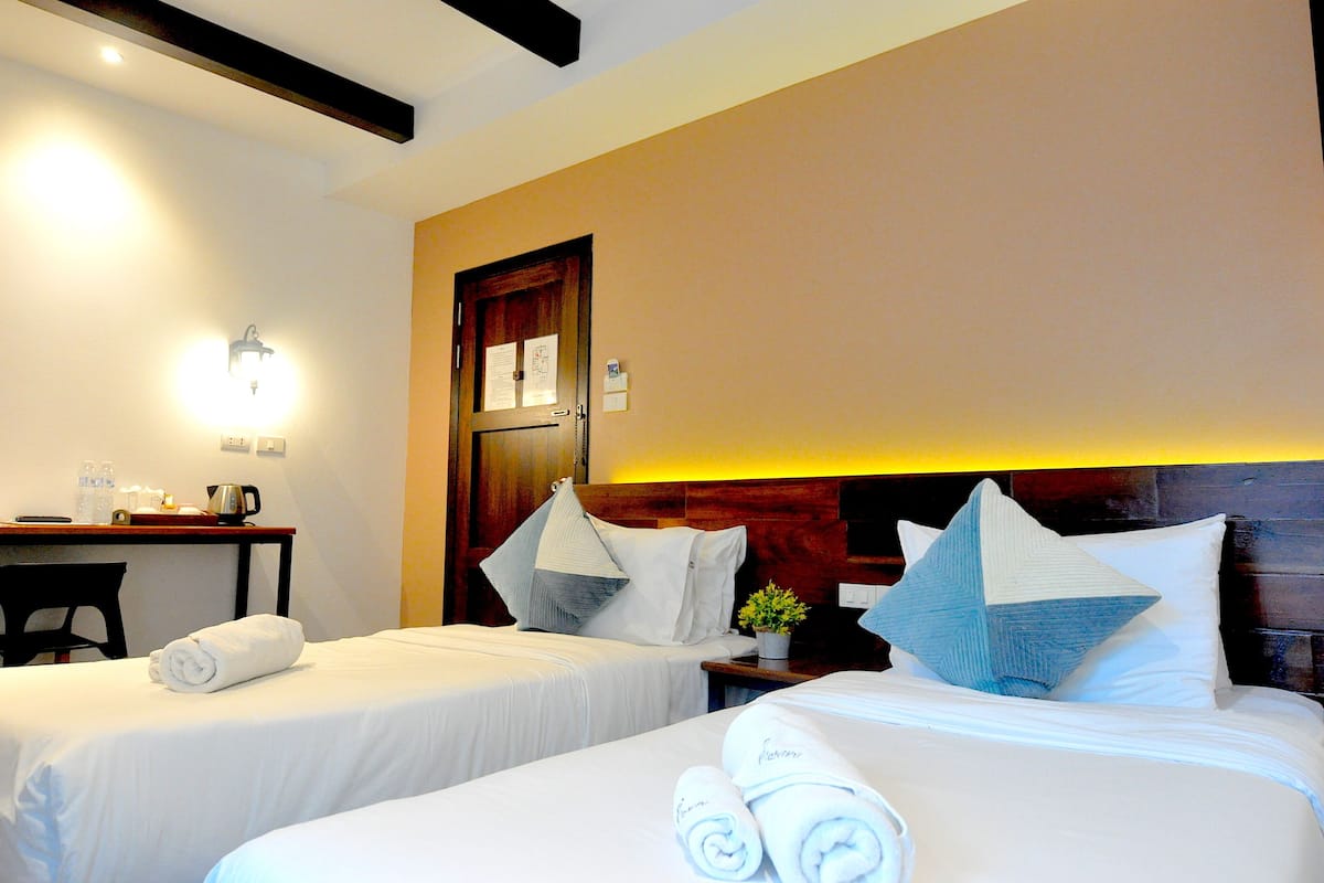 A hotel room with two beds, a desk, and a nightstand with a lamp.