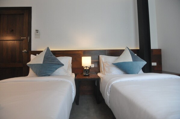 A hotel room with two beds, each with white linens and blue pillows. There is a nightstand with a lamp between the beds. - The Eight Ratvithi House (Chiang Mai)