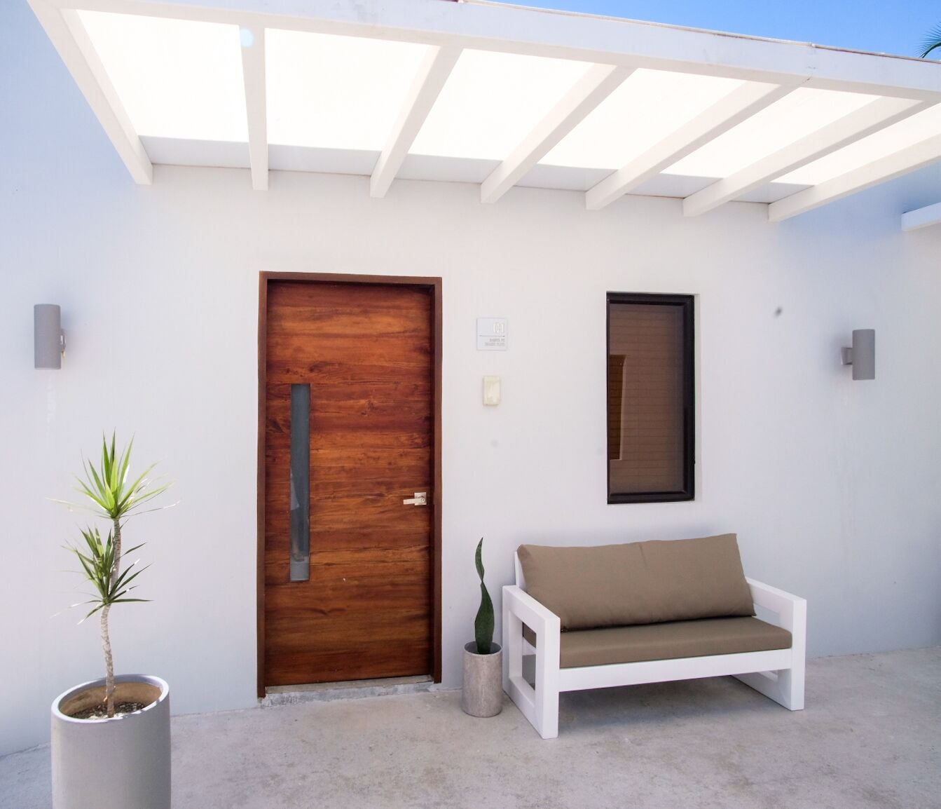 A modern outdoor seating area with a wooden door, a white bench, and a potted plant.